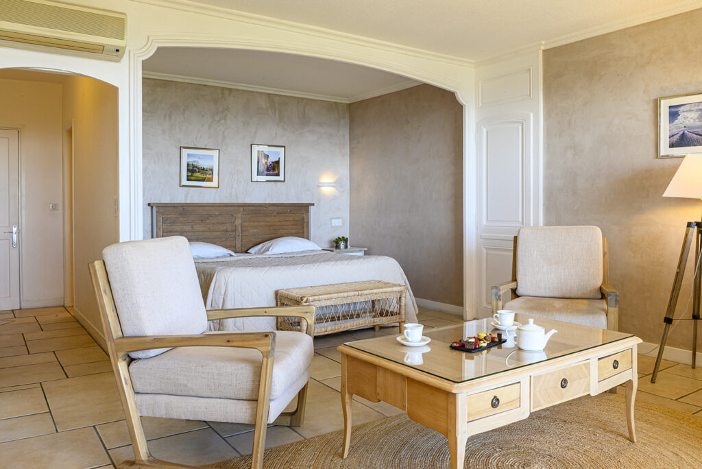 A bedroom at the Bastide de Tourtour with a bed and, in the foreground, a chair and a coffee table
