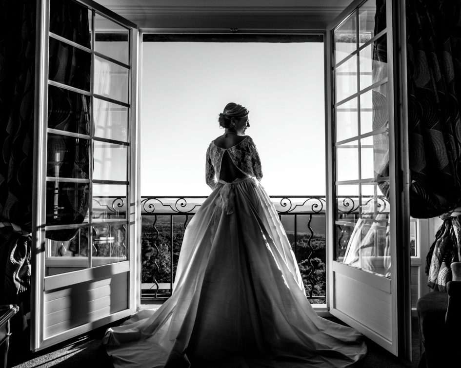 Mariée en robe qui pose devant des portes vitrées ouvertes avec vue panoramique - Bastide de Tourtour